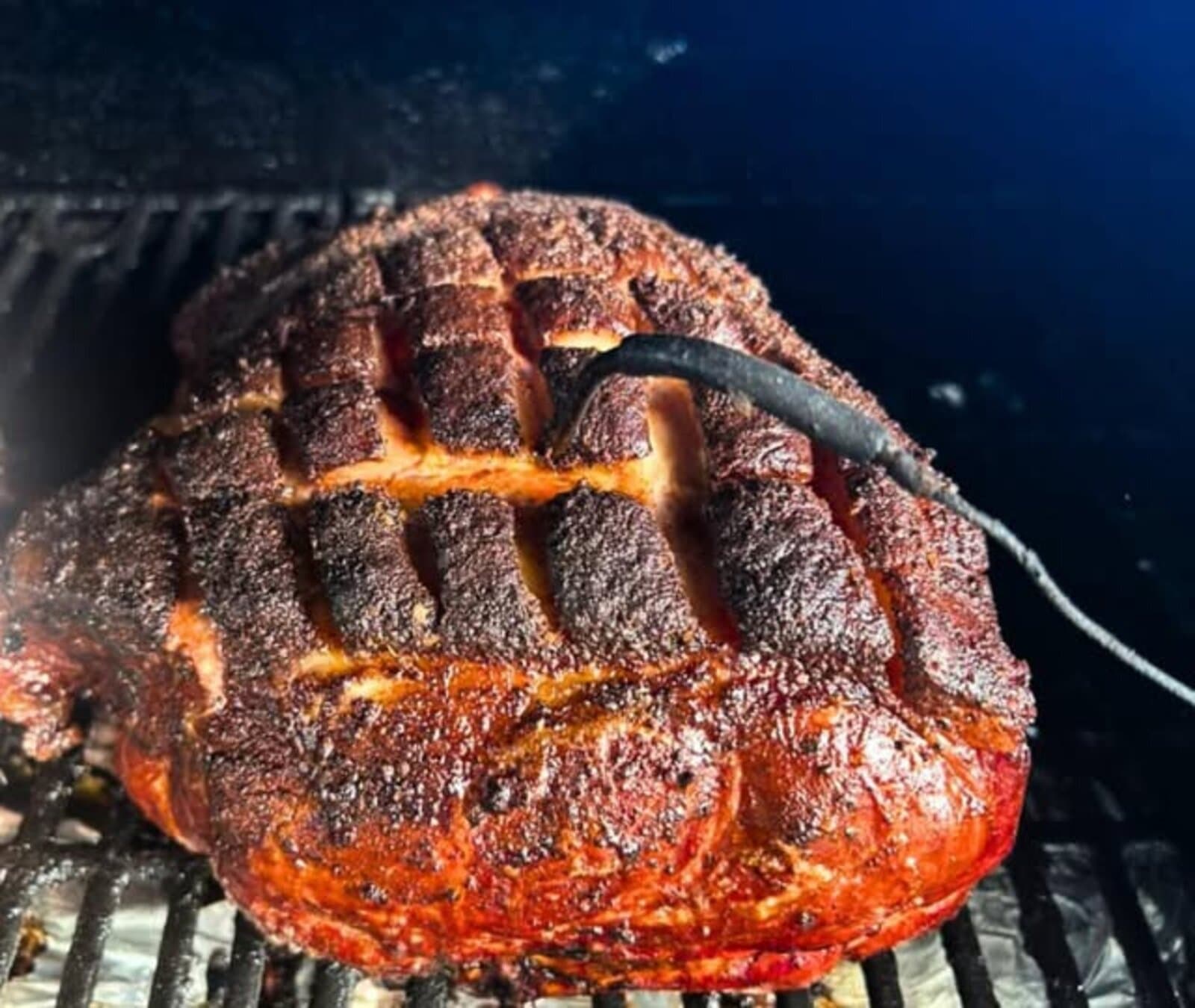Scored pork shoulder smoking on the grill